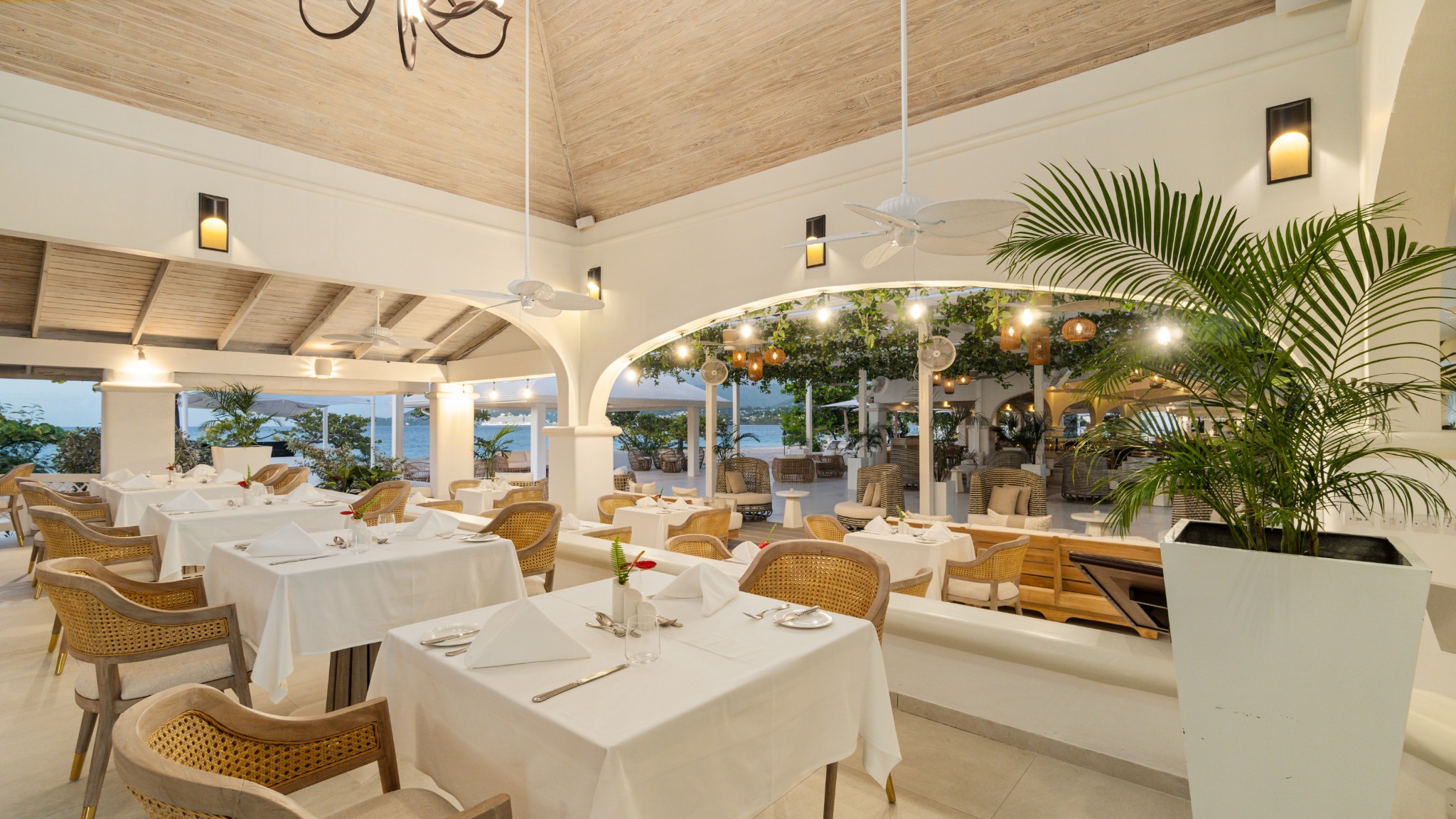 Open-sided restaurant with linen-set tables, rattan chairs and a vaulted timber ceiling