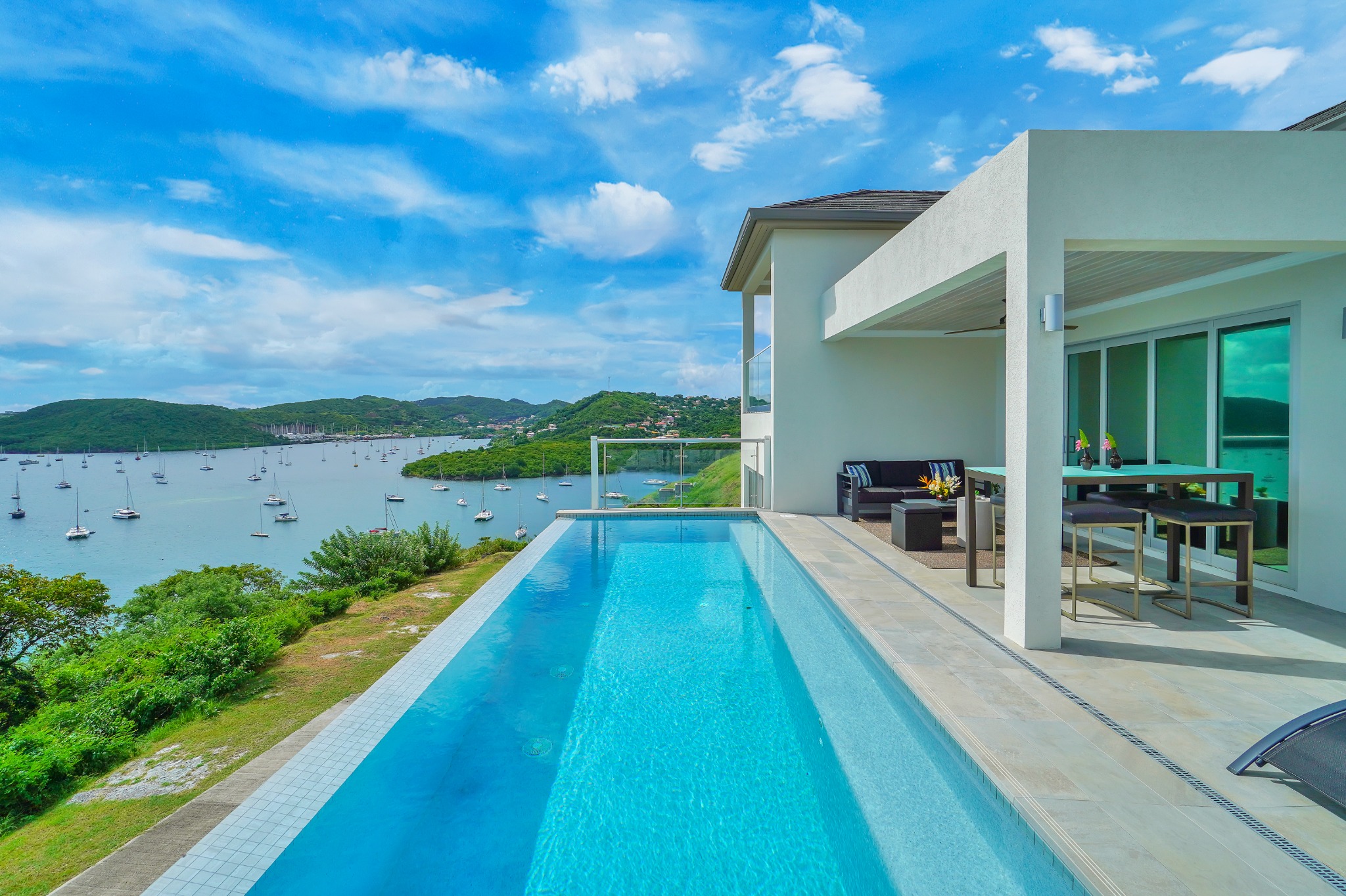 Modern hillside villa with a long blue pool overlooking a bay full of moored sailboats